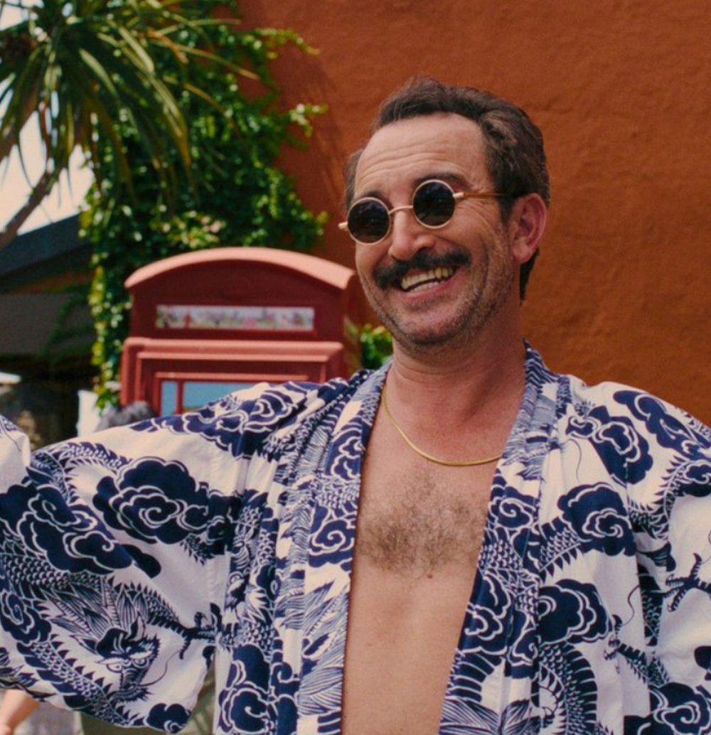 Andrew grins in round sunglasses and an open patterned shirt