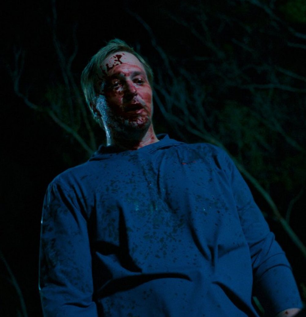 A bloodied man in the dark woods